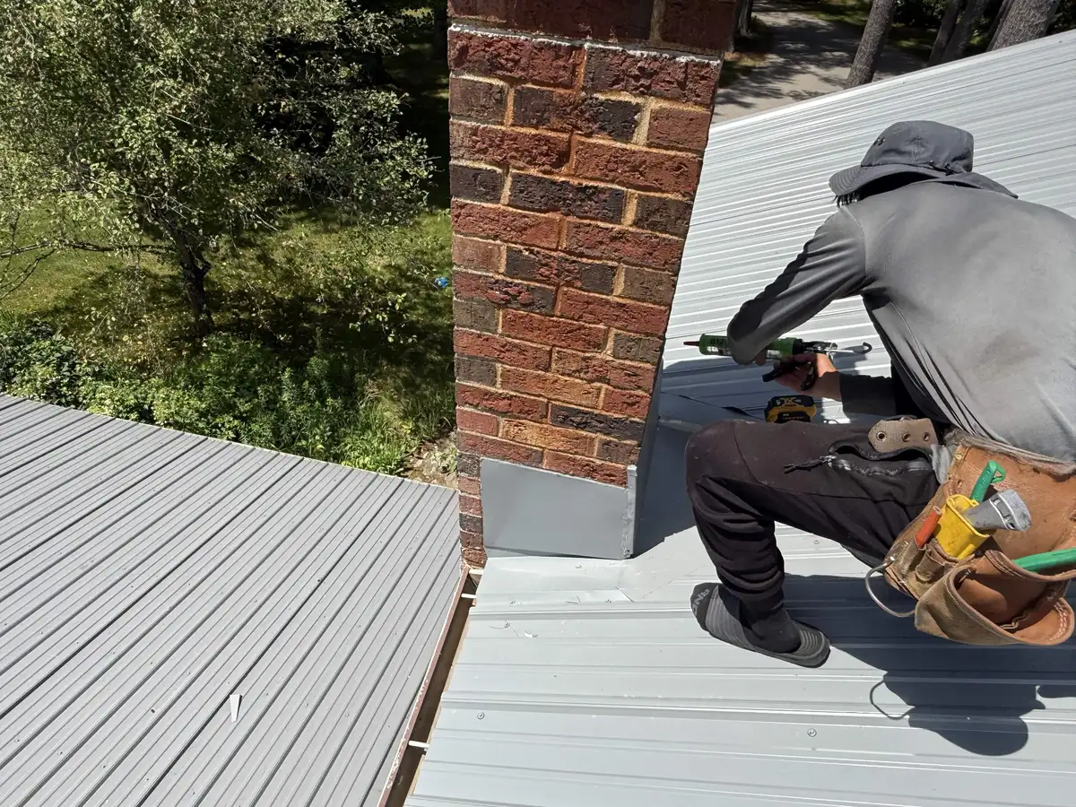 Roofer sealing new chimney flashing on a metal roof